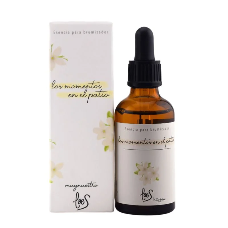 En la imagen aparece a la izquierda la caja de la Esencia Los Momentos en el Patio, con su icono de flor de azahar, nos lleva a las noches de verano. Es un aroma que huele a azahar. Abajo aparece el logo de Loes y arriba el nombre de la misma. A la derecha el bote de la bruma con el tapón tipo pipeta y la etiqueta con el mimo diseño que la caja.