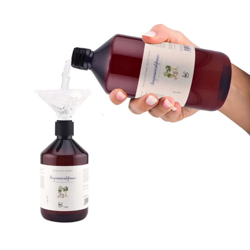 Mano de Mujer rellenando envase de 500ml con la recarga de litro del spray de tejidos con un embudo.