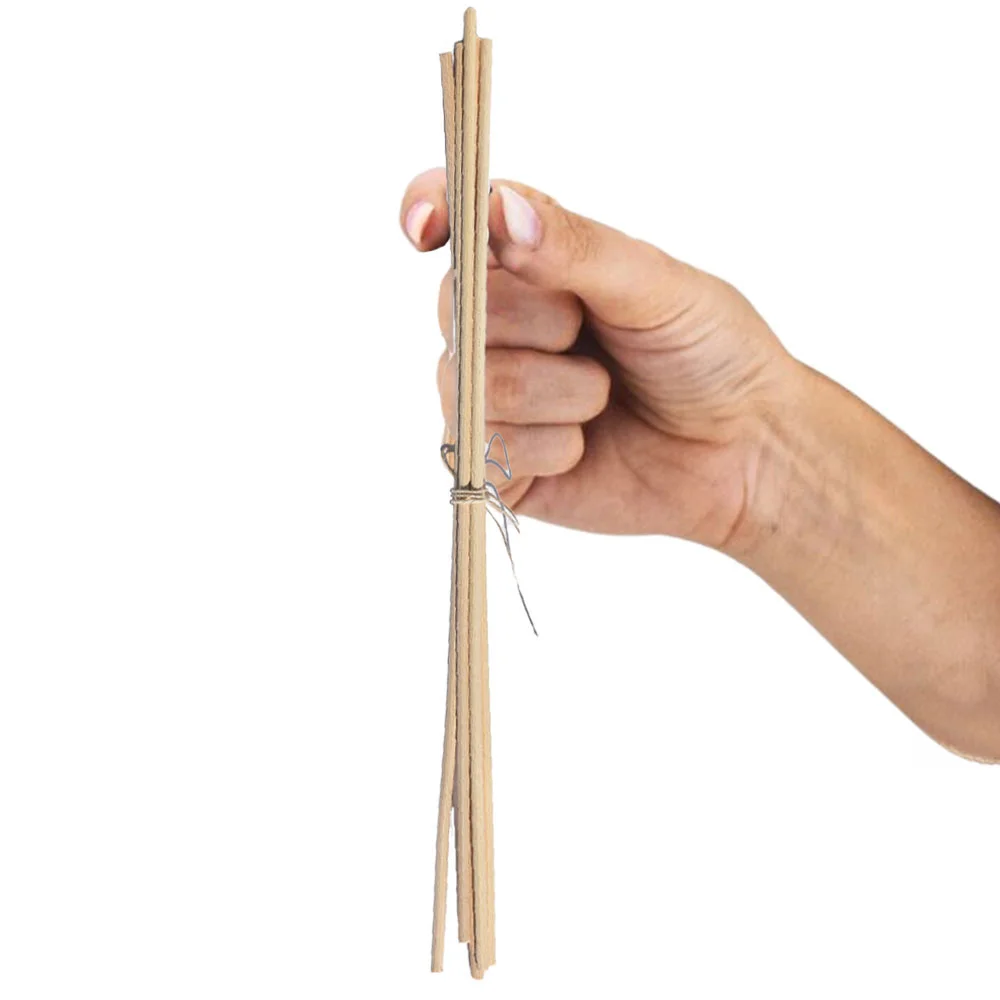 Varillas de rattán para ambientador Mikado. Cogidas por una mano de mujer sujetadas con dos dedos.