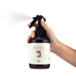 Spray de tejidos Flores en el Pelo de 500ml en la mano de una mujer dispersando el aroma floral.