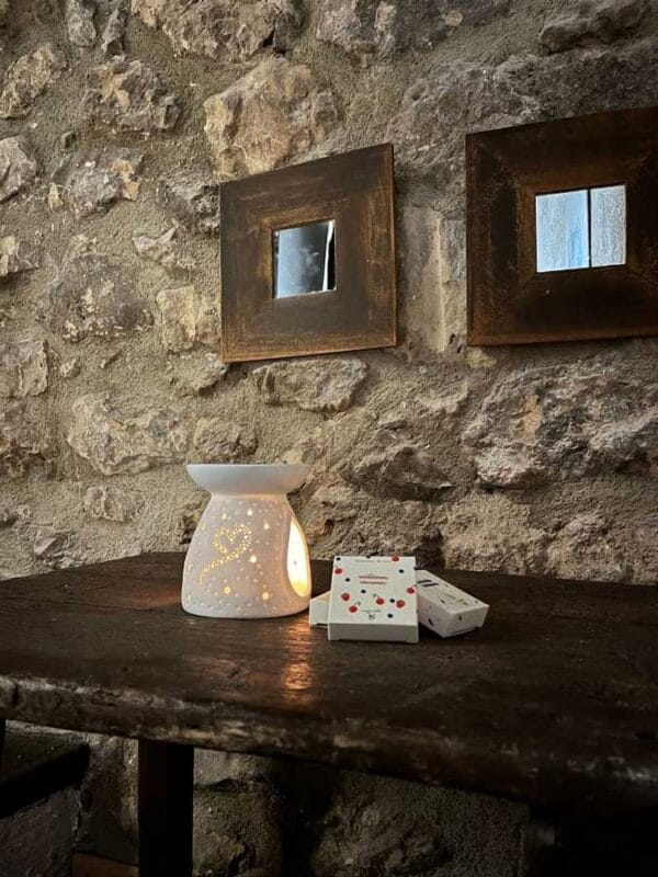 Quemador corazón encendido sobre una mesa en entorno rústico y cajitas de tartas de cera al lado.