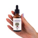 Frasco de cristal oscuro del aroma Siesta con Higos cogido con una mano de mujer y uñas arregladas.