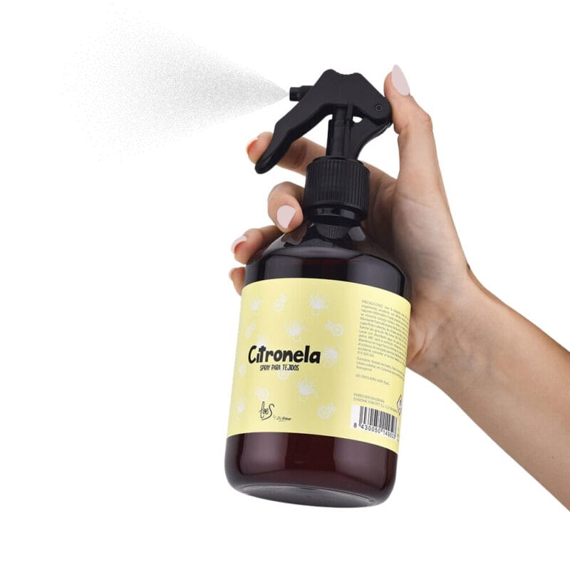 Spray para tejidos de citronela antimosquitos en la mano de una mujer pulverizando. Contiene 500ml.